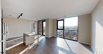 This contemporary urban residence offers a well-designed, open layout spread across a single floor, showcasing a clean modern aesthetic throughout. The living area is a standout, defined by dramatic floor-to-ceiling windows that flood the space with natural light and frame expansive views of the surrounding cityscape. Rich hardwood-style flooring runs throughout the main living and bedroom areas, complementing the neutral warm-toned walls.

The kitchen is thoughtfully outfitted with dark wood grain cabinetry, granite countertops, a decorative mosaic tile backsplash, and a full suite of stainless steel appliances including a range, dishwasher, and microwave. Track lighting overhead adds both functionality and style.

The residence includes two bathrooms, each finished with granite-topped dark wood vanities and large framed mirrors. One bathroom features a soaking tub with a tiled surround, while the other offers a glass-enclosed walk-in shower — both with clean white tile flooring.

The bedrooms benefit from the same floor-to-ceiling window design, delivering generous natural light and city views. A private balcony is accessible from the living area, providing an outdoor extension of the living space. Recessed lighting and a consistent modern design language tie the entire residence together cohesively.
