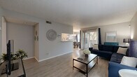 This single-story residence offers a thoughtfully designed layout encompassing one bedroom, two bathrooms, a combined dining room, kitchen, and living room, plus a closet and hallway. The open-concept living area is finished with light wood-look flooring throughout and features a textured ceiling, neutral gray walls, and a sliding glass door that invites natural light and provides access to an outdoor area. The galley-style kitchen is equipped with gray cabinetry, white countertops, black appliances including a refrigerator and electric range, and a stainless steel sink — all positioned for efficient workflow. Adjacent to the kitchen, the dining area is illuminated by a stylish multi-pendant chandelier and flows seamlessly into the living room, creating a cohesive and functional common space. The generously sized primary bedroom is carpeted for comfort and includes a ceiling fan, a window with natural light, and a dedicated closet. Two full bathrooms serve the unit, each featuring a tub-shower combination, a vanity with storage, and light flooring. Throughout the residence, the consistent use of neutral tones and modern finishes creates a clean, contemporary ambiance suited for comfortable everyday living.