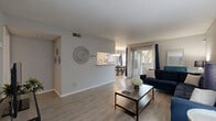 This single-story residence offers a thoughtfully designed layout encompassing one bedroom, two bathrooms, a combined dining room, kitchen, and living room, plus a closet and hallway. The open-concept living area is finished with light wood-look flooring throughout and features a textured ceiling, neutral gray walls, and a sliding glass door that invites natural light and provides access to an outdoor area. The galley-style kitchen is equipped with gray cabinetry, white countertops, black appliances including a refrigerator and electric range, and a stainless steel sink — all positioned for efficient workflow. Adjacent to the kitchen, the dining area is illuminated by a stylish multi-pendant chandelier and flows seamlessly into the living room, creating a cohesive and functional common space. The generously sized primary bedroom is carpeted for comfort and includes a ceiling fan, a window with natural light, and a dedicated closet. Two full bathrooms serve the unit, each featuring a tub-shower combination, a vanity with storage, and light flooring. Throughout the residence, the consistent use of neutral tones and modern finishes creates a clean, contemporary ambiance suited for comfortable everyday living.
