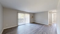 This single-floor residence offers a well-organized layout with a clean, neutral aesthetic throughout. The living area is a standout space, featuring durable wood-look plank flooring in a warm gray tone and floor-to-ceiling vertical blinds covering a large sliding glass door that fills the room with natural light and provides outdoor views. A wall-mounted air conditioning unit and a floor vent ensure year-round comfort in this open area.

The kitchen is appointed with crisp white cabinetry, marble-patterned countertops, and white appliances including a dishwasher, electric range, and overhead exhaust hood, offering a bright and functional cooking space.

The bedrooms are carpeted with plush gray carpet and feature natural light from windows with horizontal blinds. One bedroom includes a ceiling fan with light fixture for added comfort, while another offers a built-in double closet with paneled doors, providing generous storage. The rooms maintain the same neutral gray palette found throughout the home, creating a cohesive and calming atmosphere.

The dollhouse view reveals a compact, efficiently designed floor plan with a bathroom and hallway connecting the main living spaces. Overall, the residence presents a tidy, move-in-ready environment with consistent finishes and practical features across every room.