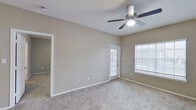 This single-floor residence offers a practical and comfortable layout designed for everyday living. The open living area is bright and welcoming, featuring neutral taupe walls, soft wall-to-wall carpeting, a ceiling fan with integrated lighting, and a large window fitted with blinds that allows natural light to fill the space. A secondary door in the living area provides convenient exterior access. The kitchen is efficiently designed with a galley-style layout, showcasing white cabinetry, granite-style countertops, wood-look flooring, and a full suite of stainless steel appliances including a refrigerator, range, and microwave. A breakfast bar connects the kitchen to the living space, enhancing the open feel. The bedroom is generously sized, carpeted for comfort, and includes a ceiling fan and a large window with outdoor views. The bathroom features white cabinetry, a granite-style vanity countertop, dual mirrors with overhead lighting, and durable wood-look flooring, with an adjacent walk-in closet offering ample storage via built-in hanging rods. A dedicated in-unit laundry area with overhead shelving completes this thoughtfully designed residence.