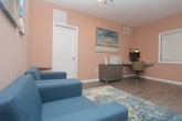 This single-floor business center is thoughtfully designed to provide a productive and welcoming environment for work and collaboration. The space features warm neutral-toned walls and light wood-style flooring throughout, creating a clean, professional ambiance.

A dedicated computer workstation along one wall is equipped with a desktop monitor and adjustable task lighting, offering a focused area for individual use. Nearby, a printer station with a storage cabinet and an abstract landscape painting above it adds both functionality and a touch of artistic character to the space.

A comfortable lounge area anchors the center of the room, featuring two contemporary teal armchairs set atop a coordinating patterned area rug, accented by sleek glass-and-wood side tables. Abstract wall art in complementary blue and neutral tones enhances the relaxed yet professional atmosphere.

Natural light filters in through multiple windows fitted with white horizontal blinds, allowing for adjustable brightness throughout the day. A high-top table with bar-style stools positioned near the windows provides an additional casual workspace ideal for short meetings or collaborative tasks.

Track lighting on the ceiling ensures consistent, well-distributed illumination across the entire space. An emergency exit sign and ventilation fixtures reflect the building's attention to safety and comfort standards.