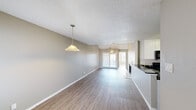 Located at 9707 Walnut Hill Ln in Dallas, Texas, this single-story, 2-bedroom, 2-bathroom home offers a well-organized layout with a comfortable, functional flow throughout. The living room serves as the centerpiece, featuring wood-look flooring, a cozy fireplace with tile surround, a ceiling fan, and a pendant light that anchors the open dining area. Natural light pours in from a glass patio door, leading to an outdoor space and creating a bright, airy ambiance. Vaulted ceilings with an arched transom window in the living area add architectural character and visual height to the space. The kitchen is equipped with crisp white cabinetry, dark granite-style countertops, black appliances including an electric range and over-the-range microwave, and a double-basin stainless steel sink. The primary bedroom features vaulted ceilings, a ceiling fan, generous natural light, and direct access to the patio. The second bedroom is well-lit with a large window. Both bathrooms include dark-topped vanities with white cabinetry, and one features a full tub-shower combination with white tile surround. Wood-look flooring runs consistently throughout, while textured ceilings add a classic finishing touch across the home.
