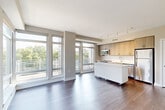 Located at 222 M St SW, Unit 501 in Washington, DC, this two-bedroom, two-bathroom residence offers a thoughtfully designed single-level layout with a comfortable and functional floor plan. The open-concept living and kitchen area serves as the heart of the unit, featuring rich hardwood flooring, track lighting, and a wall of large floor-to-ceiling windows that flood the space with natural light and provide views of the surrounding greenery. The modern kitchen is equipped with stainless steel appliances, including a full-size refrigerator and built-in microwave, complemented by warm wood cabinetry and a white kitchen island that offers additional prep and storage space. The living area flows seamlessly from the kitchen, creating an ideal space for everyday living. Both bedrooms are finished with plush carpeting and neutral-toned walls, offering a calm and restful atmosphere. The primary bedroom includes a walk-in closet with built-in shelving and convenient access to an en-suite bathroom. The bathrooms feature clean, modern finishes, including a tiled tub-shower combination, white quartz countertops, and wood-accented vanities. A hallway connects the private and shared areas of the unit, contributing to a well-organized layout throughout.