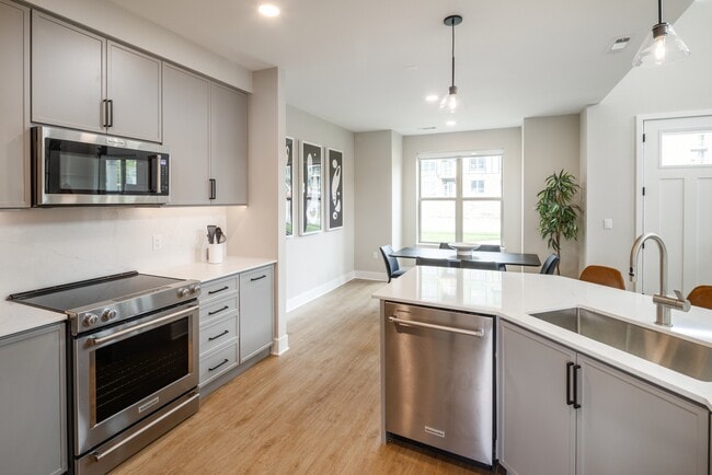 Signature Collection kitchen with stainless steel appliances, white quartz countertop, grey cabinetry, white quartz backsplash, hard surface flooring, and pendant lighting - Avalon Wayne