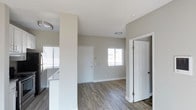 Located at 5925 El Cajon Boulevard in San Diego, Unit #310 is a single-floor residence currently vacant and move-in ready. The space showcases a clean, contemporary design with a neutral color palette of soft grays and crisp white trim that creates a bright, welcoming atmosphere throughout. The main living area features durable wood-style laminate flooring in a rich, dark tone that contrasts elegantly with the light-colored walls and white baseboards. Natural light filters in through windows fitted with horizontal blinds, keeping the space feeling open and airy. A structural column adds architectural character to the open-plan layout, subtly defining the transition between the living area and the adjacent kitchen space. The kitchen area, partially visible, includes light-toned countertops and cabinetry, offering a functional and stylish cooking environment. White interior doors with classic panel detailing provide access to additional rooms and closet storage, including a built-in closet within the main living space. Ceiling-mounted light fixtures are present throughout, ensuring consistent illumination. The overall ambiance is modern, clean, and well-maintained, making this unit a versatile and practical living space in San Diego.