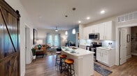This thoughtfully designed 2-bedroom, 2-bathroom residence in Panama City Beach, Florida offers a single-floor open-concept layout that blends modern functionality with coastal-inspired style. The kitchen is a standout feature, showcasing white shaker cabinetry, quartz countertops, a subway tile backsplash, stainless steel appliances, and a peninsula island with bar seating — all illuminated by pendant lighting. A dedicated pantry provides generous storage. The kitchen flows seamlessly into the living area, which features wood-style flooring, a ceiling fan, and French doors that invite natural light and outdoor access. Both bedrooms are generously proportioned, each featuring bold accent walls in deep forest green, wood-style flooring, ceiling fans, and ample natural light from large windows. The two bathrooms are finished with white cabinetry, quartz vanities, and tub-shower combinations with classic white tile surrounds. A well-lit hallway connects the private bedroom wing to the main living areas. Throughout the residence, neutral tones, wood-style flooring, and consistent finishes create a cohesive, contemporary aesthetic well-suited for comfortable coastal living.