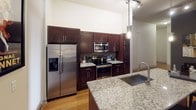 This thoughtfully designed 2-bedroom, 2-bathroom residence offers a modern living experience across a single floor. The open living area impresses with soaring ceilings, warm hardwood flooring, and generous natural light streaming through large windows fitted with roller shades. A ceiling fan adds comfort to the airy space, which comfortably accommodates distinct seating areas.

The kitchen is a standout feature, showcasing rich dark-wood cabinetry, granite countertops, a tile backsplash, stainless steel appliances including a French door refrigerator and electric range, a built-in microwave, and a large peninsula sink — ideal for both cooking and entertaining.

The primary bedroom is generously proportioned with vaulted ceilings, large windows with outdoor views, plush carpeting, and direct access to an en-suite bathroom. The primary bath offers both a soaking tub and a separate glass-enclosed shower, finished in neutral tile. An adjacent walk-in closet provides extensive wire-rack shelving for ample storage.

The second bedroom is equally well-appointed with natural light and comfortable carpeted flooring. The second bathroom features a fully tiled walk-in glass shower. Throughout, the residence maintains a clean, contemporary aesthetic with a neutral color palette and quality finishes.