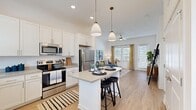 This well-designed single-floor residence offers a cohesive open-concept layout that seamlessly connects the kitchen, dining, and living areas. The kitchen is a standout feature, boasting crisp white shaker cabinetry, light quartz countertops, stainless steel appliances, and a central island with bar seating, illuminated by elegant pendant lighting. Light wood-tone flooring runs throughout, adding warmth and continuity across the space.

The living room is generously proportioned with soaring ceilings that amplify the sense of openness, and large windows dressed with drapes that allow abundant natural light to pour in. A ceiling fan adds both function and style to the space.

Two comfortable bedrooms are each fitted with multiple windows, offering excellent natural light, and feature wood-look flooring. The primary bedroom is spacious, with room for a large bed and additional furnishings.

Both bathrooms maintain the home's clean, modern aesthetic with white vanity cabinetry, quartz countertops, and wood-tone flooring. Each bathroom connects to a dedicated walk-in closet with built-in shelving, offering generous storage. One bathroom features a bathtub, while the other provides a streamlined layout ideal for everyday use. The overall ambiance is bright, airy, and thoughtfully designed.