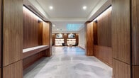 This elegantly designed single-floor commercial space strikes a compelling balance between warmth and contemporary minimalism. Throughout the space, rich walnut wood slatted wall panels serve as a defining architectural element, creating visual depth and a sense of refinement. Polished concrete floors in soft grey tones flow seamlessly across all areas, reflecting the recessed and ambient lighting overhead to enhance the spacious feel.

The main corridor is generously proportioned, flanked by tall wood-clad columns and built-in benches that offer both function and form. A skylight infuses one section of the space with a cool, blue-toned natural glow, adding an airy quality to the otherwise intimate interior. Curated artwork, including bold abstract and nature-inspired pieces, is thoughtfully integrated throughout, lending a gallery-like sensibility to the environment.

A dedicated lounge area features illuminated open shelving set within walnut millwork, displaying tasteful décor alongside framed artwork. Deep teal velvet accent chairs and a sculptural stone side table create an inviting seating vignette. A separate lounge zone offers a grey sofa, a low-profile wooden coffee table, and a striking Sputnik chandelier overhead. Crisp white paneled walls and a long, well-lit corridor complete the layout, conveying clean lines and purposeful design throughout.