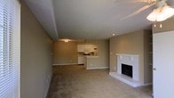 This single-floor space is designed with an open-concept layout that seamlessly connects the main living area, dining space, and kitchen. The living room is generously proportioned, finished with neutral-toned wall-to-wall carpeting that extends throughout the common areas, contributing to a warm and cohesive feel. A standout feature is the white brick fireplace, positioned along one wall of the living area, adding both a classic architectural element and a cozy focal point to the space.

The kitchen is efficiently arranged and open to the living area, anchored by a raised breakfast bar that provides a natural transition between the cooking and living spaces. White cabinetry lines the upper walls, complemented by standard appliances including an over-the-range microwave and range. A textured ceiling runs throughout the unit, adding subtle visual depth. Warm, tan-toned walls carry a consistent palette across the space, while recessed and flush-mount lighting provide adequate illumination. The overall ambiance is understated and functional, with a traditional aesthetic suited to comfortable everyday living.