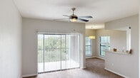Located in Austin, TX, this 2-bedroom, 2-bathroom residence offers a thoughtfully laid-out single-floor plan designed for comfortable everyday living. The living area is a standout, featuring plush carpeting, a stylish five-blade ceiling fan, and a large sliding glass door with vertical blinds that opens to a private balcony with lush green views. Natural light flows freely through multiple windows fitted with blinds throughout the space. The kitchen is open and functional, featuring wood-trimmed cabinetry with white panel doors, a double stainless steel sink, a dishwasher, and generous counter space. A pass-through window connects the kitchen to the adjoining dining area, which is accented by a pendant light fixture. Both bedrooms are carpeted and equipped with ceiling fans; the secondary bedroom includes a window with blinds, while the primary bedroom benefits from a dedicated walk-in closet with double hanging rods and shelf storage. The two bathrooms feature wood-tone cabinetry, light wood-style flooring, shower/tub combinations, and ample storage. Hallways connect the space efficiently, completing a practical and comfortable floor plan ideal for those seeking a well-appointed home in Austin.