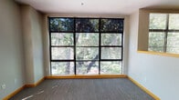 Located on the third floor at 1400 P St in midtown Sacramento, Unit 310 is a single-level residence that stands out for its impressive natural light and verdant outdoor views. The living areas are anchored by expansive floor-to-ceiling grid windows framed in dark metal, offering sweeping views of mature trees that create a serene, nature-filled ambiance throughout the unit. Plush carpeting and warm wood baseboards run consistently across the living and bedroom spaces, contributing to a cohesive and comfortable feel.

The kitchen is thoughtfully designed with light wood cabinetry accented by matte black hardware, dark laminate countertops, a double stainless steel sink, and a full suite of appliances including a refrigerator, electric range, and microwave. A raised peninsula separates the kitchen from the carpeted living area, while a skylight overhead brightens the cooking space with additional natural light.

An exterior door with a sidelight panel provides access to an outdoor area, further connecting the unit to its leafy surroundings. The bathroom features wood-look vinyl flooring, a light wood vanity with a large mirror, and a tub-shower combination. Overall, the unit offers a calm, functional layout well-suited to everyday living in the heart of Sacramento.