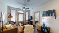 This single-story residence offers a thoughtfully designed layout with distinct living, dining, kitchen, and sleeping areas. The living room serves as the central gathering space, featuring rich dark hardwood-style flooring, a ceiling fan, and an entry door framed by windows fitted with blinds and sheer curtains that allow ample natural light. Built-in shelving and an open sightline to the bedroom beyond enhance the room's functional flow.

The kitchen is outfitted with dark espresso cabinetry extending to the ceiling, granite-style countertops, stainless steel appliances including a refrigerator and range, and a dishwasher. A breakfast bar provides additional counter space and casual seating.

The bedrooms are carpeted and feature ceiling fans, large windows with blinds and sheer curtains, and generous closet access. The primary bathroom includes dark wood vanity cabinetry, a wide granite-topped countertop, an oversized mirror, and direct access to a spacious walk-in closet. The overall aesthetic throughout the unit is consistent—neutral walls paired with dark finishes create a clean, contemporary ambiance.