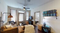 This single-story residence offers a thoughtfully designed layout with distinct living, dining, kitchen, and sleeping areas. The living room serves as the central gathering space, featuring rich dark hardwood-style flooring, a ceiling fan, and an entry door framed by windows fitted with blinds and sheer curtains that allow ample natural light. Built-in shelving and an open sightline to the bedroom beyond enhance the room's functional flow.

The kitchen is outfitted with dark espresso cabinetry extending to the ceiling, granite-style countertops, stainless steel appliances including a refrigerator and range, and a dishwasher. A breakfast bar provides additional counter space and casual seating.

The bedrooms are carpeted and feature ceiling fans, large windows with blinds and sheer curtains, and generous closet access. The primary bathroom includes dark wood vanity cabinetry, a wide granite-topped countertop, an oversized mirror, and direct access to a spacious walk-in closet. The overall aesthetic throughout the unit is consistent—neutral walls paired with dark finishes create a clean, contemporary ambiance.