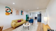 This thoughtfully designed 2-bedroom, 1-bathroom residence makes excellent use of its single-floor layout, combining functionality with a clean, modern aesthetic. Light hardwood flooring flows seamlessly throughout, tying together each room with warmth and continuity.

The living room serves as the heart of the space, featuring recessed lighting, bright white walls, and natural light from a window with blinds. Bauhaus-inspired artwork adds a contemporary artistic flair, complementing the open sightline into the kitchen and dining area.

The kitchen is well-appointed with stainless steel appliances — including a range, microwave, and dishwasher — paired with dark lower cabinetry, white upper cabinets, quartz countertops, and a classic subway tile backsplash. A window above the sink brings in natural light.

Both bedrooms are comfortably sized, each equipped with a ceiling fan, recessed lighting, and light-filtering window blinds. The primary bedroom benefits from a window with an outdoor view, while the second bedroom features a framed cityscape print, adding a distinctive character to the space.

A hallway connects the rooms efficiently, and the unit also includes a dedicated laundry area. The overall ambiance is bright, clean, and modern — ideal for comfortable everyday living.