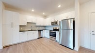 Located at 1040 Clearwater Largo Rd N in Largo, Florida, this single-floor unit offers a clean, contemporary design with thoughtful finishes throughout. The kitchen serves as a central highlight, outfitted with crisp white shaker-style cabinetry extending to the ceiling for ample storage, a subtle tile backsplash, dark countertops, and a full suite of stainless steel appliances including a refrigerator, electric range, built-in microwave, and dishwasher. Light wood-look flooring runs throughout the kitchen and living areas, contributing to a bright, cohesive aesthetic complemented by recessed lighting overhead.

The living area is generously proportioned, featuring a ceiling fan and direct access to a private balcony through a glass door flanked by windows, allowing natural light and outdoor views to enhance the space. The bedrooms are finished with plush carpet flooring, ceiling fans, and natural light from windows with blinds. Closet space is provided via bifold-door closets with built-in shelving. The bathroom is finished with large-format wood-grain tile surrounding the tub and shower, coordinating floor tile, a white vanity with dark countertop, and clean, modern fixtures throughout.