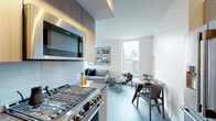 This well-appointed high-rise residence offers a refined contemporary living experience across a single floor. The open-concept layout seamlessly connects the kitchen, dining, and living areas, creating an expansive, fluid space ideal for both everyday living and entertaining. Floor-to-ceiling windows flood the living room with natural light and frame impressive city skyline views, complementing the clean white walls and dark hardwood flooring throughout.

The chef's kitchen is outfitted with premium stainless steel appliances, including a professional-grade gas range, built-in microwave, French door refrigerator, and dishwasher. Warm wood cabinetry, a tile backsplash, and a generously sized countertop complete this highly functional culinary space. A dedicated dining area sits adjacent, accommodating comfortable everyday meals.

The two bedrooms are carpeted and serene, each offering ample space and access to city views. The bathroom features a sleek, extended vanity with stone countertops, an undermount sink, and a large mirror, reflecting a minimalist and sophisticated design sensibility. A dedicated laundry area with a stacked washer and dryer adds everyday convenience. Throughout, the residence maintains a cohesive modern aesthetic defined by neutral tones, quality finishes, and thoughtful design.