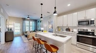 This thoughtfully designed 2-bedroom, 2-bathroom single-floor residence offers a comfortable and modern living experience. The open-concept kitchen and living room serve as the heart of the home, featuring light wood-style flooring, recessed lighting, and a seamless flow between spaces. The kitchen is outfitted with white shaker cabinetry, a subway tile backsplash, stainless steel appliances including a range, microwave, refrigerator, and dishwasher, and a large center island with a white quartz countertop, undermount sink, and pendant lighting — ideal for both meal prep and casual dining with bar seating. The living area is bright and welcoming, with natural light streaming through large windows and a sliding door. The primary bedroom is a generously sized retreat featuring plush carpet, a bold accent wall, and large windows with outdoor views. It is served by a private en-suite bathroom with a walk-in shower, single vanity with ample storage, and wood-look tile flooring. The second bedroom mirrors the primary in style and comfort. The second bathroom features a soaking tub with tiled surround, a wide vanity, and matching flooring. A dedicated in-unit laundry room with a full-size washer and dryer adds everyday convenience. Two closets provide additional storage throughout.