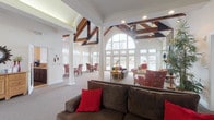 Located at 1 Village Gate Blvd in Delaware, Ohio, this single-story community clubhouse offers an impressive and welcoming environment designed for both relaxation and social interaction. The centerpiece of the space is a dramatic great room featuring soaring vaulted ceilings with bold, exposed dark wood beam trusses and a stunning arched window wall that floods the interior with natural light and provides sweeping views of the outdoor pool area. French doors offer seamless access to the exterior, enhancing the sense of openness throughout.

The main gathering area is generously proportioned, accommodating multiple seating arrangements with ease. A striking floor-to-ceiling stone fireplace with a rustic wood mantel anchors one side of the room, adding warmth and character. Adjacent to the great room, a welcoming lounge area greets visitors with comfortable seating and a warm, residential feel.

A dedicated computer room provides built-in cabinetry, an extended work surface with multiple workstations, and ample upper storage — ideal for resident use. The well-appointed galley kitchen features rich dark wood cabinetry, tile countertops, full appliances including a range and refrigerator, and generous storage throughout. Together, these spaces create a functional and inviting community hub suited to a variety of activities and gatherings.