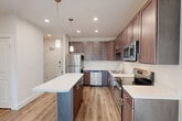 This well-appointed one-bedroom, one-bathroom unit in South Burlington, Vermont offers a thoughtfully designed layout across a single floor. The open-concept living, dining, and kitchen area serves as the heart of the home, featuring wide-plank wood-style flooring that flows throughout the space. The kitchen is equipped with rich dark-brown shaker-style cabinetry, white quartz countertops, a full suite of stainless steel appliances including a refrigerator, electric range, microwave, and dishwasher, and a central island with pendant lighting overhead — ideal for both meal prep and casual dining. The living area is bright and airy, with a large window that invites natural light and offers views of surrounding trees. The bedroom is a comfortable, well-sized retreat featuring a double-door closet and its own window with natural views, complemented by the same light wood-style flooring. The bathroom is finished with dark wood cabinetry, a single vanity with a wide mirror, a glass-enclosed shower, and a tall linen tower for added storage. Additional highlights include three closets throughout, a dedicated laundry area, and a welcoming entry hallway. Recessed lighting and a clean, neutral color palette lend a modern, move-in-ready feel to the entire unit.
