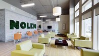 This single-floor space is designed as a contemporary communal lounge or lobby area, blending industrial and modern aesthetics to create a welcoming, functional environment. The most distinctive feature is the eye-catching wall display of large letters spelled out in preserved moss, mounted against an exposed brick backdrop painted in a light grey tone, adding a bold, biophilic focal point to the space.

The ceiling is left exposed, revealing ductwork and structural elements typical of industrial design, while a combination of pendant drum lights and linear fluorescent fixtures ensures the space is well-lit. Large windows along one side of the room invite substantial natural light, enhancing the overall brightness and openness of the interior.

The seating is arranged in multiple groupings, featuring light chartreuse upholstered armchairs and sofas paired with dark wood coffee tables, creating distinct conversation zones. Additional dining-style seating with orange chairs and wooden tables occupies one corner, offering a more casual setting. A wall-mounted flat-screen television is positioned near the center, adding a functional media element. Light hardwood flooring and a natural fiber area rug complete the clean, contemporary aesthetic.