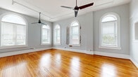 Located in the heart of downtown Spartanburg, SC, this 2-bedroom, 2-bathroom residence blends historic architectural character with modern updates. Throughout the single-floor layout, rich hardwood floors gleam under abundant natural light, setting a warm and inviting tone. Striking arched windows are a defining architectural feature, appearing in multiple rooms and flooding the space with daylight while offering views of the surrounding area. Exposed brick accents add texture and a nod to the building's heritage, complementing the soft gray walls and crisp white trim found throughout.

The open living area is generously proportioned, with high ceilings and ceiling fans enhancing the sense of volume and airflow. The hallway showcases elegant beadboard wainscoting, adding classic detail to the transition between rooms. The kitchen is outfitted with dark cabinetry, stainless steel appliances including a French door refrigerator, granite countertops, and subway tile backsplash, with an arched window providing natural light.

Both bedrooms are well-sized and share the same warm hardwood floors, arched windows, and exposed brick character. The spacious primary bedroom offers a generous footprint. The bathrooms feature refined finishes, including marble-topped dark vanities, hexagonal tile flooring, and large-format tile tub surrounds with brushed bronze fixtures.
