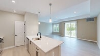 This well-appointed single-floor unit offers a thoughtfully designed layout that maximizes functionality and comfort. The open-concept kitchen and living area serves as the heart of the space, featuring light wood-tone cabinetry paired with white upper cabinets, a subway tile backsplash, stainless steel appliances including a gas range, microwave, refrigerator, and dishwasher, and a large center island with quartz countertops and pendant lighting overhead. Recessed lighting and light hardwood-style flooring run throughout, creating a bright, cohesive aesthetic. The living area opens directly to a private balcony through sliding glass doors, bringing in abundant natural light and outdoor views.

The bedroom is a comfortable size, featuring a ceiling fan, a wide window overlooking greenery, and a dedicated closet. The bathroom includes a wood-tone vanity with white quartz countertop, an undermount sink, and matte black hardware accents that tie in with the rest of the unit's modern design. A dedicated laundry room houses a full-size washer and dryer with built-in shelving. The entry foyer provides a welcoming transition into the unit with clean lines and neutral tones throughout.