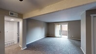 This single-floor unit offers a practical and functional layout designed for comfortable everyday living. The main living area is generously sized, featuring neutral gray walls, plush wall-to-wall carpeting, and a structural beam detail overhead that adds architectural character. A sliding glass door floods the space with natural light and opens to a private balcony with exterior views. An adjacent area, defined by a partial wall, extends the living space and connects seamlessly to the entryway, which features durable hard-surface flooring for easy maintenance.

The kitchen is well-appointed with crisp white cabinetry, stone-look countertops, a stainless steel sink, and a built-in dishwasher. Open shelving above the range provides additional display or storage space.

The bedrooms are carpeted and offer a calm, neutral palette with adequate natural light from standard windows fitted with blinds. Each room provides sufficient space for furnishings and includes closet access via paneled doors.

The bathroom is finished with a stone-look vanity countertop and wood-look flooring, lending a clean, updated appearance. Throughout the unit, white baseboards provide a crisp contrast to the warm taupe wall tones, contributing to a cohesive and move-in-ready aesthetic.