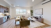 This well-appointed studio offers a smart, open-concept layout that maximizes every square foot across a single floor. Light-toned, wood-look plank flooring flows seamlessly throughout, lending warmth and visual continuity to the entire space. The living area is bright and airy, anchored by large windows that invite generous natural light and provide open outdoor views, creating a relaxed and welcoming ambiance. Recessed lighting complements the natural light overhead, while a wall-mounted mini-split system ensures year-round comfort. A dedicated sleeping area integrates naturally within the open plan, allowing for flexible furniture arrangements. The kitchen is a standout feature, outfitted with rich wood-grain cabinetry extending floor to ceiling, a crisp white quartz countertop, a double stainless steel sink, and a full suite of stainless steel appliances including a range, microwave, and dishwasher — ideal for everyday cooking. Ample pantry and closet storage is provided by a bank of clean, white shaker-style built-in cabinetry near the entryway. The bathroom is finished in a minimalist style with light wood vanity cabinetry, a white quartz countertop, and a full shower-tub combination, all set against bright white walls and matching wood-look flooring for a cohesive, modern feel.