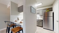 This single-story space is thoughtfully designed with a cohesive neutral palette, light wood-style flooring, and an airy ambiance carried throughout. The kitchen is a functional highlight, featuring grey cabinetry, white subway tile backsplash, light stone countertops, and stainless steel appliances including a refrigerator and microwave. A peninsula with bar seating for two creates a natural transition into the dining and living areas, making it ideal for casual meals or entertaining.

The living room is bright and welcoming, with large windows that invite natural light and offer views of greenery outside. A glass-paned door provides additional outdoor access. The space feels open and versatile, with clean wall finishes and durable flooring continuing throughout.

The bedroom is comfortably sized, featuring a ceiling fan with light, windows with exterior views, and direct access to a walk-in closet outfitted with hanging storage. The layout offers practical privacy and organization.

The bathroom is finished with large-format tile in the tub surround, light wood-look flooring, a grey vanity, and clean white fixtures, creating a calm, spa-like feel. Overall, the space presents a modern yet approachable aesthetic with consistent, quality finishes.