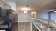 This single-floor residential unit is thoughtfully designed with a clean, modern aesthetic and consistent wood-look flooring that flows throughout the entire space. The open-concept layout connects the kitchen and living area seamlessly, creating a welcoming and functional common space. The kitchen is well-appointed with gray cabinetry, granite-style countertops, a subway tile backsplash, a stainless steel sink, and black appliances including an electric range and refrigerator. A peninsula counter separates the kitchen from the living area, which is anchored by a pendant light fixture and provides ample room for everyday living and dining.

A long hallway leads to the private areas of the unit, which include multiple bedrooms. Each bedroom features ceiling fans, neutral gray walls, and wood-look flooring. One bedroom benefits from a window that allows natural light to fill the space, while an adjacent walk-in closet offers generous storage with wire shelving and hanging rods.

Two bathrooms serve the unit, each featuring dark-framed mirrors, gray vanity cabinetry, and matching countertops. One bathroom includes in-unit laundry hookups, adding everyday convenience. White trim and baseboards throughout contribute to the space's clean, cohesive look, while neutral wall tones create a calm, move-in-ready atmosphere.