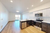 Located at 3118 6th Ave in Tacoma, WA, this modern one-bedroom, one-bathroom unit offers a well-designed open-concept layout across a single floor. Light hardwood flooring flows throughout, creating a cohesive and contemporary feel.

The kitchen serves as a central focal point, featuring dark wood lower cabinetry contrasted by crisp white upper cabinets, a white quartz countertop, a peninsula with an integrated sink, and a full suite of stainless steel appliances including a range, microwave, dishwasher, and refrigerator. Recessed lighting and a white tile backsplash complete the modern aesthetic.

The kitchen opens seamlessly into the living area, which is bathed in natural light through large sliding glass doors that lead to a private balcony — ideal for enjoying outdoor views of the surrounding neighborhood.

The spacious primary bedroom offers generous proportions with clean white walls, hardwood flooring, and ample room for furnishings. It connects conveniently to the full bathroom, which includes a single-sink vanity with dark wood cabinetry, a white countertop, a large mirror, and a tub/shower combination. The clean, neutral palette across all rooms gives the unit a bright, move-in-ready appeal.