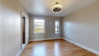 Located at 1050 N Sherman St in Denver's Capitol Hill neighborhood, this efficient one-bedroom, one-bathroom unit offers a well-organized layout across a single floor. The main living and sleeping area is generously sized relative to the overall footprint, featuring warm hardwood flooring that runs throughout and two windows that allow natural light to fill the space while offering views of the surrounding Denver streetscape. A ceiling-mounted fan-light fixture provides both ventilation and illumination. A built-in storage unit with open shelving, a mirrored cabinet, and integrated drawers offers practical organization directly within the bedroom area. The compact kitchen is accessible through a dedicated doorway and is outfitted with light wood cabinetry, dark countertops, a stainless steel refrigerator, and a microwave. The classic black-and-white checkered tile floor gives the kitchen a distinctive, timeless character. The bathroom features traditional hexagonal mosaic tile flooring, white penny-tile wainscoting, a pedestal sink, a bathtub, and warm wood cabinetry above the toilet. A solid dark wood door adds a touch of classic craftsmanship. The unit's neutral gray and beige tones throughout create a clean, functional, and cohesive aesthetic.