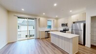 This well-appointed three-story home offers a thoughtfully designed layout across three distinct levels. The ground floor provides a garage, entrance, and additional living space with light-toned luxury vinyl plank flooring, recessed lighting, and a staircase leading to the upper levels. The main living floor serves as the heart of the home, featuring an open-concept kitchen and living room filled with natural light. The kitchen is outfitted with light wood cabinetry, white quartz countertops, stainless steel appliances including a refrigerator, range, microwave, and dishwasher, and a central island ideal for casual dining or meal prep. Sliding glass doors open to a balcony, extending the living space outdoors. The upper floor hosts all three bedrooms, including a generously sized primary bedroom with plush carpeting, a walk-in closet with wire shelving, and natural light from well-placed windows. The additional bedrooms are carpeted and bright. Five bathrooms are distributed throughout the home, featuring clean, modern fixtures including glass-panel tub-shower combinations with brushed nickel hardware. A dedicated laundry room with a full-size washer and dryer adds everyday convenience. Consistent use of light tones, recessed lighting, and quality finishes give the entire home a fresh, modern ambiance.