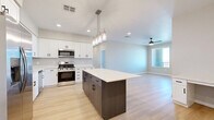 Located at 39695 W Lococo St in Maricopa, AZ, this single-story, 4-bedroom, 2-bathroom home offers a clean, modern aesthetic with thoughtfully designed living spaces. The open-concept kitchen and living area serves as the heart of the home, featuring white shaker-style cabinetry with black hardware, bright white quartz countertops, a bold navy-accented center island with pendant lighting, and a full suite of stainless steel appliances including a refrigerator, range, microwave, and dishwasher. Light wood-style flooring flows throughout the main living areas, lending warmth and continuity to the space. The living room is bright and airy, bathed in natural light from large windows and accented by a ceiling fan overhead. The four bedrooms are finished with plush neutral carpet and feature windows that invite natural light, with some offering open desert views. Both bathrooms are well-appointed with white cabinetry, quartz vanity tops, black hardware accents, and wood-style flooring. One bathroom includes a walk-in shower with built-in shelving. A dedicated closet adds convenient storage. The home's neutral color palette and consistent modern finishes create a cohesive, move-in-ready feel throughout.