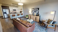 This single-floor residence showcases a contemporary industrial aesthetic defined by striking exposed concrete ceilings that extend throughout the living areas and bedrooms, creating a raw yet refined architectural character. The open-concept living and dining area is anchored by large floor-to-ceiling windows and a glass-panel balcony door, flooding the space with natural light while offering expansive panoramic city views. The balcony provides a private outdoor retreat directly accessible from both the living room and bedroom.

The kitchen is well-appointed with stainless steel appliances, including a gas range, built-in microwave, and French door refrigerator. A sleek white peninsula with an integrated sink provides generous counter space and accommodates bar seating for casual dining. Cabinetry combines crisp white upper cabinets with darker lower units for visual contrast, while wood-look flooring flows throughout the main living areas.

The bedrooms continue the industrial-modern theme with exposed concrete ceilings and large sliding glass doors leading to the balcony, maximizing natural light and outdoor views. The bathroom features clean, minimalist finishes including a dark wood vanity, white countertop, and light tile flooring, maintaining a cohesive contemporary palette throughout the residence.