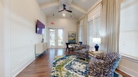 Located at 900 Graces Reserve Circle in Concord, NC, this single-floor community space combines thoughtful architectural design with a bold, contemporary aesthetic. Soaring vaulted ceilings with exposed beams and ceiling fans lend an airy, open feel to the main lounge area, which is bathed in natural light streaming through large windows dressed with elegant floor-to-ceiling drapes and classic wood blinds. Rich hardwood flooring flows seamlessly throughout the entire space, grounding the vibrant interior design.

The lounge area serves as a welcoming gathering spot, anchored by a striking jewel-toned area rug and bold zebra-print accent chairs arranged around a small round bistro table — perfect for casual conversation or a quiet moment. A wall-mounted flat-screen TV and a sleek console provide functional amenities alongside the decorative touches.

Glass French doors open directly to the outdoors, flooding the space with additional light and providing convenient exterior access. Toward the interior, a dedicated workspace area features a full-sized desk with computer workstations, ideal for productivity. An adjacent room, visible through a wide doorway and lit by a chandelier, offers additional flexible space. Curated artwork and lush decorative plants add personality and warmth, making this a refined and functional community destination.