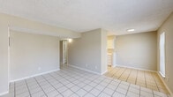 This single-floor, 2-bedroom, 1-bathroom unit offers a straightforward and functional layout designed to maximize its footprint. The open living area features large white ceramic tile flooring and neutral-toned walls, creating a clean and bright atmosphere. A textured popcorn ceiling runs throughout the common areas, lending a classic residential feel. The kitchen, partially visible from the living room, includes white cabinetry and continues the tile flooring for easy maintenance.

Both bedrooms are carpeted for comfort and equipped with ceiling fans with light fixtures, providing both ventilation and illumination. The primary bedroom is notably spacious and benefits from multiple closets, offering generous storage options. Natural light filters in through windows fitted with horizontal blinds. The second bedroom also features carpeted flooring, a ceiling fan, and a window with an outdoor view.

The bathroom is clean and functional, featuring a full-size tub and shower combo with white surrounds, tile flooring, and essential fixtures. Three closets are distributed throughout the unit, providing ample storage. The overall color palette is soft and neutral, with warm beige and white tones creating a cohesive, understated ambiance throughout the space.