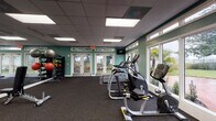 Located at 1658 S Hiawassee Rd in Orlando, Florida, this single-floor fitness center is a well-equipped exercise facility designed to support a full range of workout routines. The space features teal-painted walls and a drop-panel ceiling with recessed fluorescent lighting, creating a bright and energizing atmosphere throughout.

The cardio section is outfitted with multiple treadmills, elliptical machines, and a stationary bike, all positioned near large windows and glass double doors that flood the area with natural light and offer views of the surrounding outdoor greenery, including palm trees. A wall-mounted television is also present for entertainment during workouts.

The strength training area includes a multi-station cable and weight machine, a leg press, and a well-stocked dumbbell rack with a full range of free weights. Exercise balls, medicine balls, resistance bands, and additional accessories are neatly organized on dedicated storage racks, supporting functional and group fitness training.

Full-length mirrors line portions of the walls, enhancing the sense of space and allowing users to monitor their form. Rubber flooring throughout provides durability and safety underfoot. The facility also includes a water fountain and restroom access, ensuring user convenience. Overall, this fitness center offers a comprehensive and inviting environment for health and wellness activities.