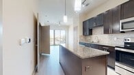 This 570-square-foot, one-bedroom, one-bathroom apartment is thoughtfully laid out across a single floor, maximizing functionality within a compact footprint. The open-concept kitchen is a standout feature, equipped with dark espresso cabinetry, granite countertops, a stainless steel appliance suite including a refrigerator, range, microwave, and dishwasher, and a tiled backsplash. A kitchen island with pendant lighting and track lighting overhead enhances both the aesthetics and utility of the space. Light wood-style flooring runs throughout the main living and kitchen areas, contributing to a clean, modern aesthetic. The 110-square-foot bedroom features plush wall-to-wall carpeting, neutral wall tones, and a large window fitted with horizontal blinds, allowing for ample natural light and outdoor views. The full bathroom is finished with large-format tile flooring, a dark-cabinet vanity with a granite countertop, and a tiled soaking tub with a shower. A door from the bathroom leads directly into a dedicated walk-in closet, which is outfitted with multi-level shelving and hanging rods for generous storage. Built-in wall shelving in the kitchen area adds additional display and storage options, completing this efficient and well-appointed apartment.