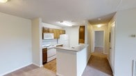 Located at 201 Eads Street in East Ridge, Tennessee, this single-floor residence offers a practical and comfortable layout designed for everyday living. The kitchen serves as a central hub of the home, featuring warm wood-toned cabinetry that provides generous storage space. White appliances, including a range, microwave, and refrigerator, are seamlessly integrated into the design. A peninsula-style counter extends into the living area, creating a natural transition between the kitchen and the adjoining carpeted living space, while also offering additional prep and seating space. The flooring in the kitchen transitions to hardwood-style material, adding a touch of warmth and easy maintenance underfoot. A hallway leads from the main living area to additional rooms, suggesting a thoughtful separation of private and communal spaces. The interior is finished with neutral-toned walls and ceilings, allowing for versatile décor choices. Recessed cabinetry and a closet visible along the hallway contribute to the overall storage capacity of the home. The layout flows efficiently throughout, making this a well-organized and functional single-level living space in the East Ridge community.