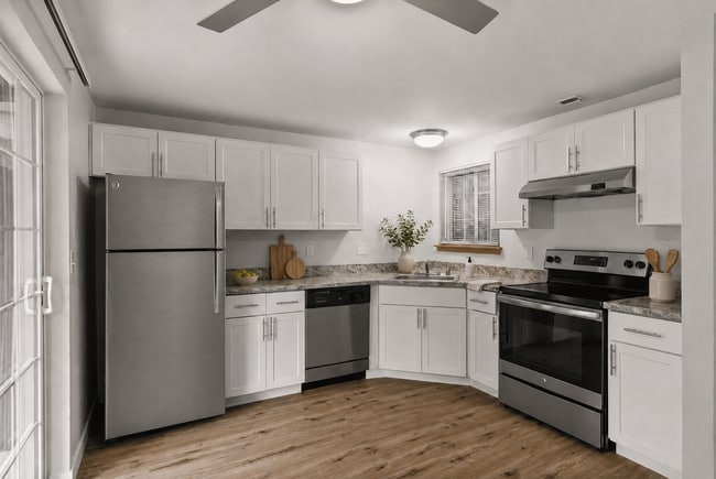 Staged apartment kitchen with white cabinetry, stainless-steel appliances, wood-look flooring, greenery, and modern countertop décor. - Stonegate Apartments