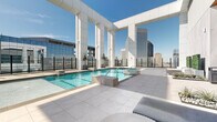 Located in the heart of downtown Houston at 808 Crawford St, this exceptional rooftop pool deck offers a premier elevated outdoor experience high above the city. The space is defined by its sleek, modern architectural design, characterized by bold white structural columns, large-format light stone tile flooring, and floor-to-ceiling glass perimeter railings that preserve unobstructed, panoramic views of the Houston skyline and surrounding metropolitan area.

The centerpiece of the deck is a generously sized swimming pool with crystal-clear blue water, complemented by a separate spa or wading area for added relaxation. Lounge cabanas with green hedge accents line the poolside, providing shaded retreat areas, while contemporary modular outdoor seating arrangements create inviting social spaces throughout the terrace. Potted trees and carefully curated greenery add natural contrast to the crisp white palette of the architecture.

The glass barrier system enclosing the perimeter ensures safety without compromising the breathtaking elevated vistas, which include prominent Houston landmarks and the broader city skyline. A semi-enclosed indoor-outdoor amenity structure with warm wood accents and floor-to-ceiling glazing anchors one end of the deck, providing a sheltered complement to the open-air areas. The overall ambiance is sophisticated, airy, and resort-inspired, offering an exceptional urban retreat above downtown Houston.