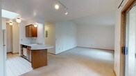 Located at 3003 S Perry St in Spokane, Washington, this single-floor unit offers a practical and comfortable layout designed for everyday living. The open-concept living and dining area is finished with plush neutral carpet and features a vaulted ceiling section, track lighting, and a pass-through kitchen counter that creates a seamless connection between the kitchen and living space. The kitchen is equipped with wood-toned cabinetry, a coil-burner electric range, a refrigerator, and light countertops with tile flooring, providing all the essentials for meal preparation. The spacious living room receives generous natural light through a large vertical-blind window, creating a bright and welcoming atmosphere, with baseboard heating ensuring year-round comfort. The bedrooms are carpeted and well-sized, with one featuring a wall-mounted air conditioning unit and a window overlooking the surrounding neighborhood, while another includes a walk-in closet for ample storage. The full bathroom is finished with classic white tile surrounding a full soaking tub and shower combo, complemented by patterned tile flooring, a baseboard heater, and a vanity with storage. Throughout the unit, clean white walls and warm wood trim accents contribute to a tidy, move-in ready aesthetic.