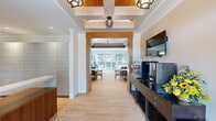 This thoughtfully designed single-floor amenity space offers a generous layout that seamlessly blends function and style across its interconnected areas. The entry corridor sets an elegant tone with coffered ceilings accented by warm wood inlays, decorative pendant lighting, and light hardwood flooring that flows consistently throughout the space.

A dedicated reception and package room features a handsome walnut-toned desk, wall-to-wall parcel lockers, and recessed lighting, providing a polished and highly organized experience. Adjacent to the entry, a beverage station outfitted with a Nespresso machine, mini-refrigerator, and fresh floral arrangements creates a welcoming hospitality touch.

The lounge area is bright and comfortable, with large windows framed by floor-length gray drapes that invite natural light and views of surrounding greenery. Leather armchairs, a glass coffee table, a patterned area rug, and a wall-mounted television complete this relaxed gathering space. A dining nook with a glass-top table and warm wood chairs provides a quiet setting for meetings or casual meals.

The fully equipped kitchen features white shaker cabinetry, stainless steel appliances, a mosaic tile backsplash, and a central island with quartz countertops and leather barstools beneath a trio of sculptural teal pendant lights.

At the rear, a wall of folding glass doors opens entirely to a landscaped outdoor patio with seating and shade structures, creating an effortless indoor-outdoor connection filled with natural light.