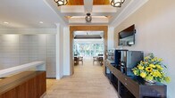 This thoughtfully designed single-floor amenity space offers a generous layout that seamlessly blends function and style across its interconnected areas. The entry corridor sets an elegant tone with coffered ceilings accented by warm wood inlays, decorative pendant lighting, and light hardwood flooring that flows consistently throughout the space.

A dedicated reception and package room features a handsome walnut-toned desk, wall-to-wall parcel lockers, and recessed lighting, providing a polished and highly organized experience. Adjacent to the entry, a beverage station outfitted with a Nespresso machine, mini-refrigerator, and fresh floral arrangements creates a welcoming hospitality touch.

The lounge area is bright and comfortable, with large windows framed by floor-length gray drapes that invite natural light and views of surrounding greenery. Leather armchairs, a glass coffee table, a patterned area rug, and a wall-mounted television complete this relaxed gathering space. A dining nook with a glass-top table and warm wood chairs provides a quiet setting for meetings or casual meals.

The fully equipped kitchen features white shaker cabinetry, stainless steel appliances, a mosaic tile backsplash, and a central island with quartz countertops and leather barstools beneath a trio of sculptural teal pendant lights.

At the rear, a wall of folding glass doors opens entirely to a landscaped outdoor patio with seating and shade structures, creating an effortless indoor-outdoor connection filled with natural light.