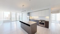 Located at 45 Lansing Street in the heart of San Francisco, this modern 3-bedroom, 1-bathroom residence offers a thoughtfully designed open-concept layout with high-end finishes throughout. The combined kitchen and living area serves as the centerpiece of the home, showcasing a sleek, contemporary kitchen equipped with stainless steel appliances, a gas range, built-in oven, and a large central island with integrated shelving. White lacquered upper cabinetry is paired with rich dark wood lower cabinets, creating a striking two-tone aesthetic. Light-toned plank flooring and recessed lighting complete the polished look. Floor-to-ceiling windows flood the living area with abundant natural light and frame dramatic views of the San Francisco skyline and bay beyond. The three bedrooms continue the modern aesthetic, featuring soft carpeting and expansive window walls that offer sweeping high-rise city views. The primary bedroom is generously sized, providing a comfortable and private retreat. The bathroom is finished with large-format marble-style tile in both the shower surround and flooring, complemented by a modern wall-mounted sink and a combined tub and shower. Throughout, the residence maintains a clean, minimalist design philosophy with bright white walls and an abundance of natural light.