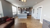 This well-appointed single-floor residence offers a thoughtfully designed open-concept layout that seamlessly connects the living, dining, and kitchen areas. The living room features warm wood-look flooring, a ceiling fan, and a generous arrangement of windows fitted with blinds that invite abundant natural light while providing exterior views.

The kitchen is a standout feature, anchored by a central island with a white countertop and sink, and outfitted with rich dark-toned cabinetry, stainless steel appliances including a refrigerator, electric range, and over-the-range microwave, as well as a classic white subway tile backsplash. Track and pendant lighting add a modern touch overhead.

Adjacent to the kitchen, a louvered bifold door reveals a convenient in-unit laundry closet with a full-size washer and dryer. The bedrooms are carpeted for comfort, each equipped with ceiling fans and windows that bring in natural light. Closet space is well provided, with a dedicated walk-in closet visible from the hallway.

Both bathrooms maintain a consistent, clean aesthetic with dark wood vanities, white countertops, wood-look flooring, and neutral gray walls. Throughout the residence, the cool gray color palette, white trim, and black hardware accents create a cohesive, contemporary style.