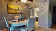 This well-appointed single-floor residence offers a comfortable and cohesive layout designed for everyday living. The open-concept living and dining area serves as the heart of the home, anchored by a fireplace, ceiling fan, and a wall-mounted television. Plush carpeting flows throughout the space, complemented by warm, neutral tones on the walls. A sliding glass door floods the dining area with natural light and provides direct access to a private patio overlooking mature greenery, creating a seamless indoor-outdoor connection. The dining space comfortably accommodates a round table with upholstered seating, ideal for gatherings.

The kitchen features rich, dark cabinetry, a mosaic tile backsplash, dark countertops, and hardwood-style flooring, with a peninsula that opens toward the main living area. A full suite of appliances completes this functional culinary space.

The bedrooms are generously sized, each offering plush carpeting, large windows with blinds and draping curtains, and stylish accent walls that lend a distinctive character to each room. Natural light is a consistent theme throughout the home.

A hallway bath is conveniently positioned between the main living spaces and the bedrooms, rounding out this well-balanced and inviting residence.